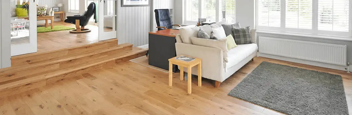 A modern living room with professionally installed laminate flooring, a beige sofa, a small side table, a gray rug, and large windows with white shutters in Erie, PA